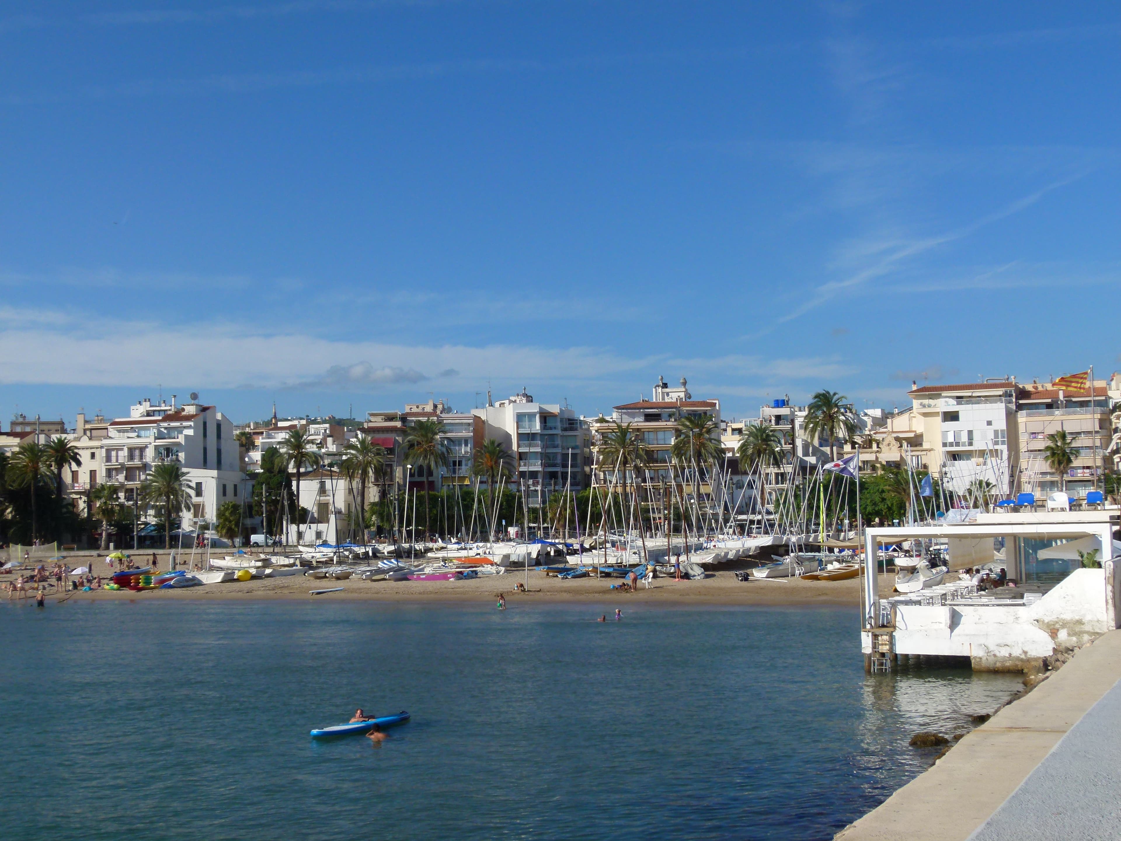 Areia dourada e guarda-sóis da Platja de la Ribera com a orla de Sitges ao fundo