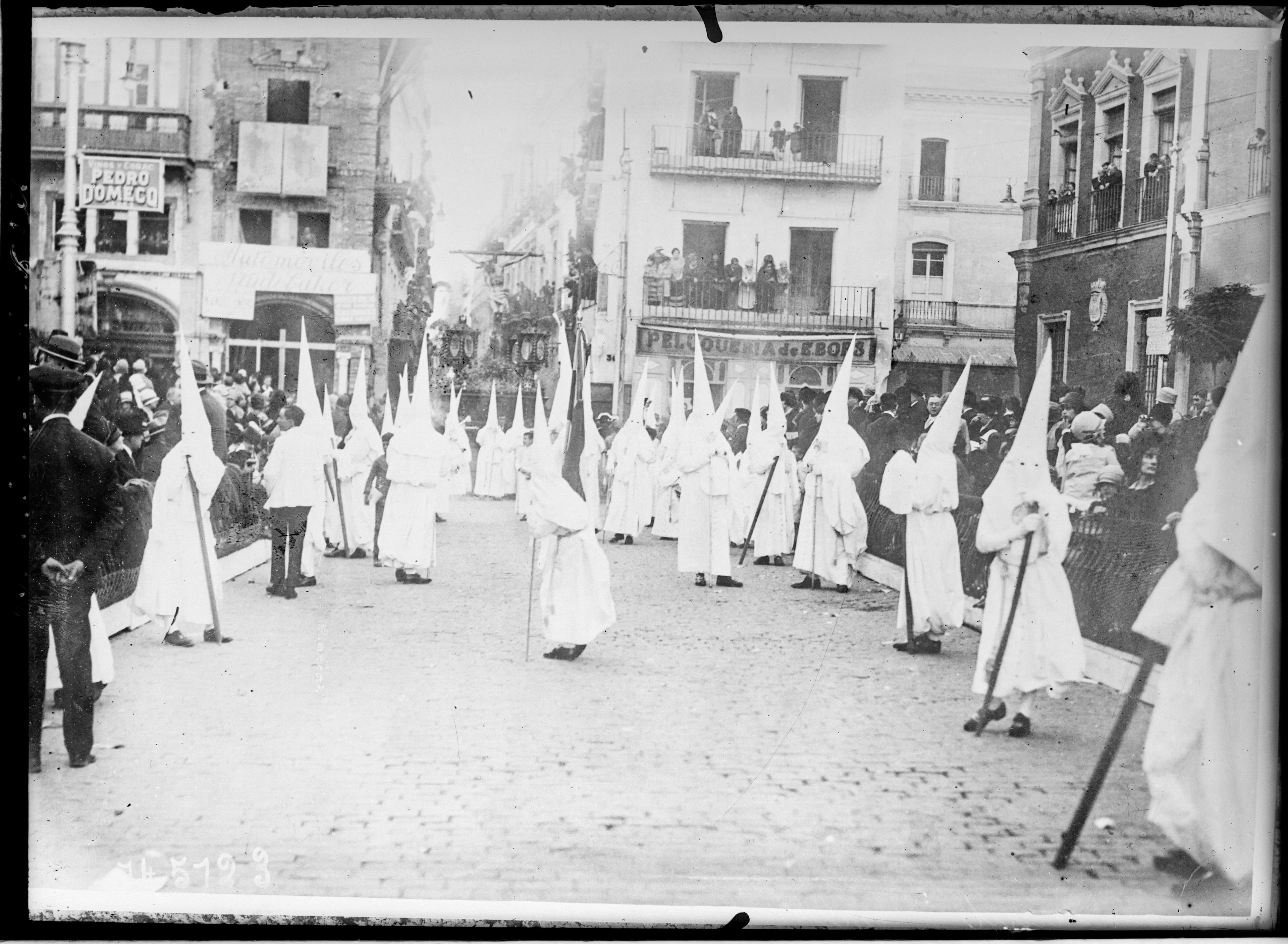 Grupo de nazarenos con capirote desfilando por la Plaza de San Francisco de Sevilla durante la Semana Santa, fotografía de 1930