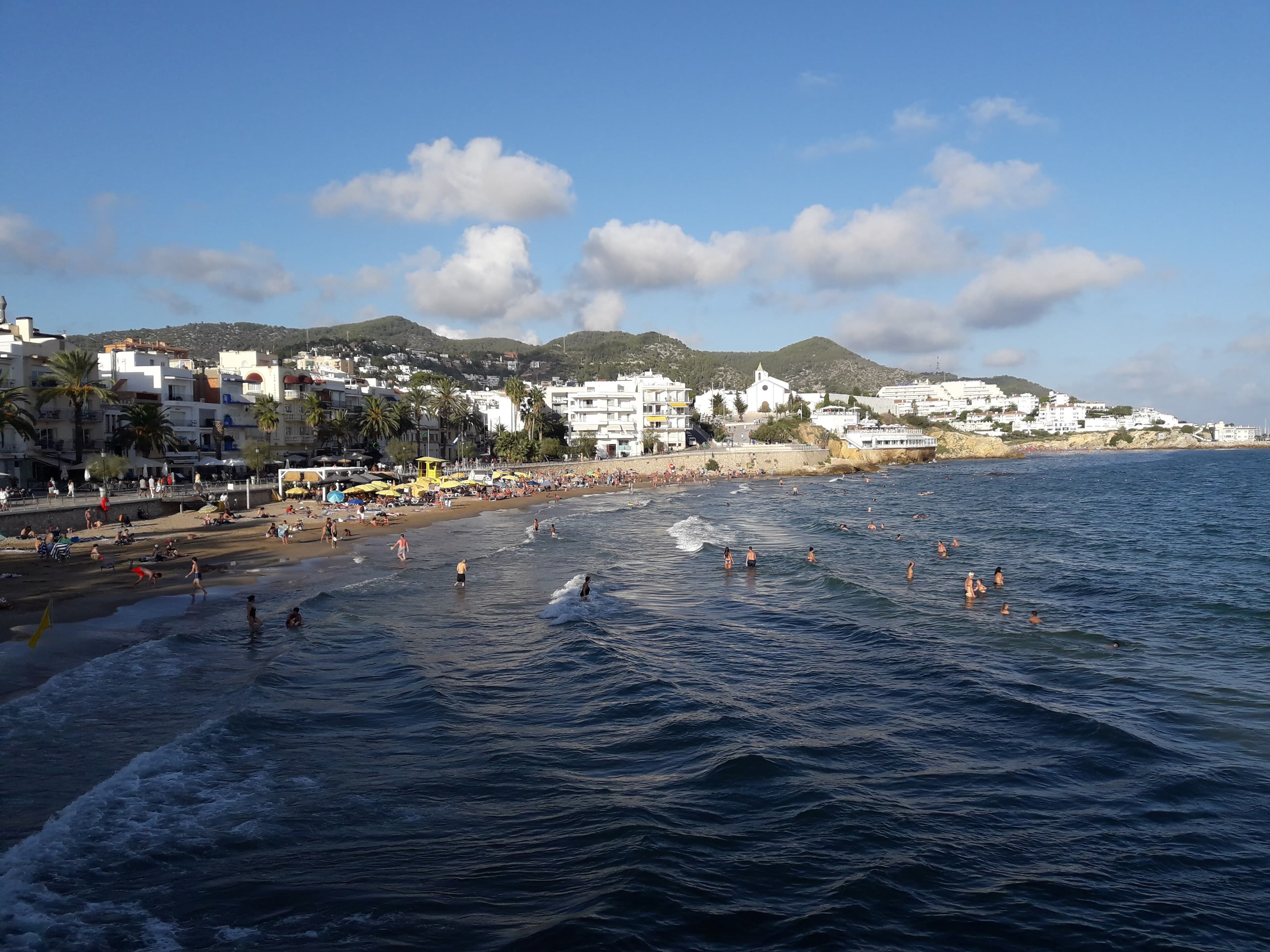 A tranquila Platja de Sant Sebastià de Sitges com barcos encalhados e o campanário ao fundo